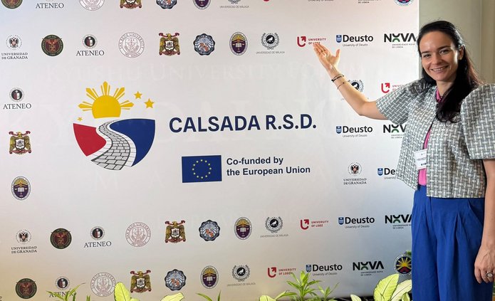 a woman standing in front of a backdrop displaying institutional logos