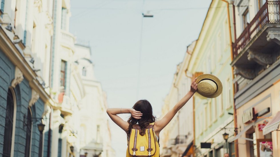 Back view of a young woman traveler with a backpack on her shoul Dziewczyna na wakacjach zwiedza miasto z kapeluszem w ręce